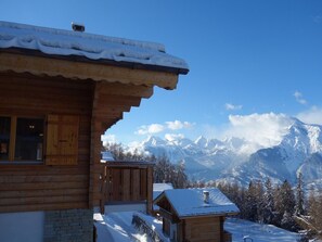 Una cabaña de madera con techo nevado y vistas a montañas cubiertas de nieve.