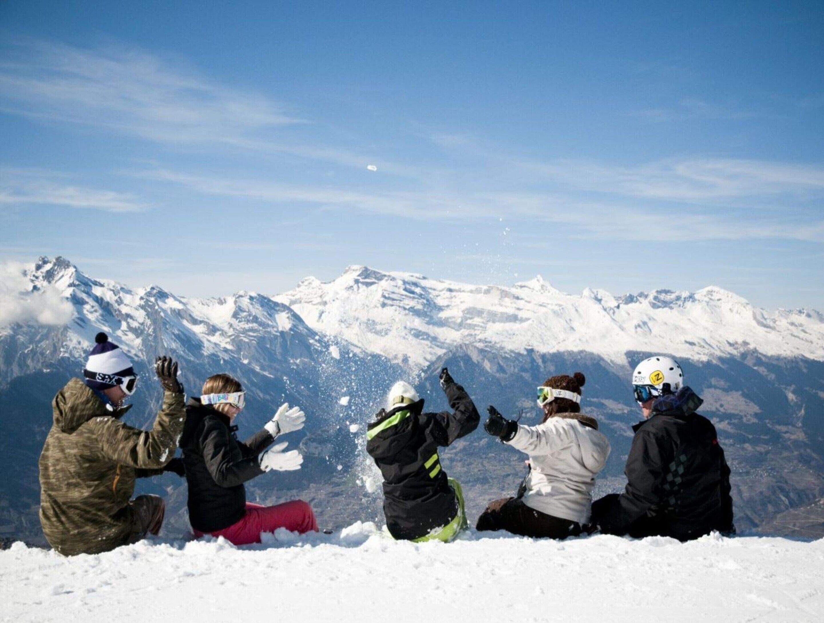 Un grupo de personas sentadas en una montaña nevada, con picos cubiertos de nieve al fondo.