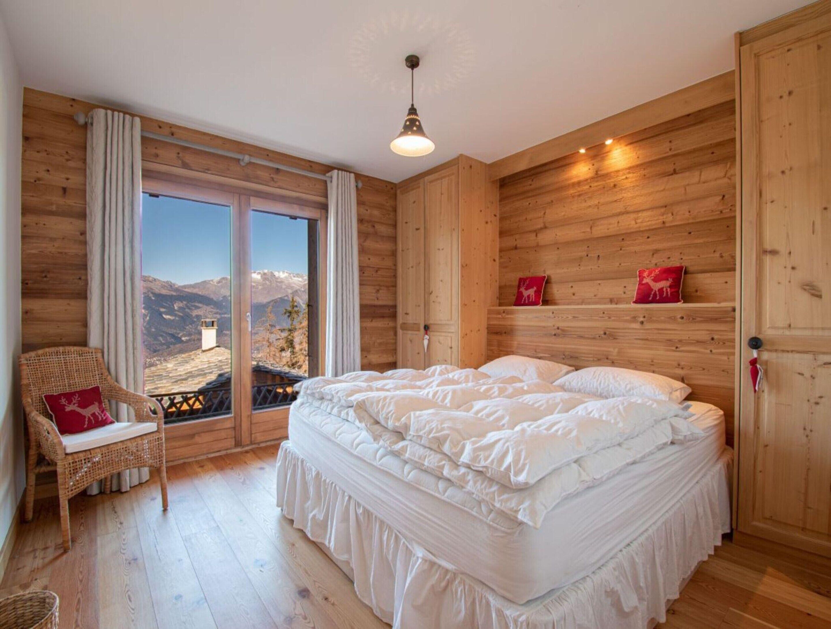 A bedroom with a large bed, wooden walls, a wicker chair, and a view of mountains.