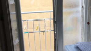 Una habitación con ventana que da a un balcón con barandilla de metal y pared amarilla.
