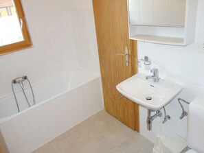 A bathroom with a bathtub, a sink, and a wooden door. - Cozy Apartment for Groups (Sion)
