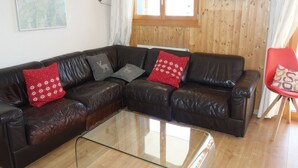 A living room with a brown leather sectional sofa, a glass coffee table, and a red chair. - Cozy Apartment for Groups (Sion)