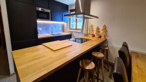 A modern kitchen with black cabinets, a wooden countertop, a stainless steel range hood, and a window with a view of trees. - Cozy Apartment for Groups (Sion)