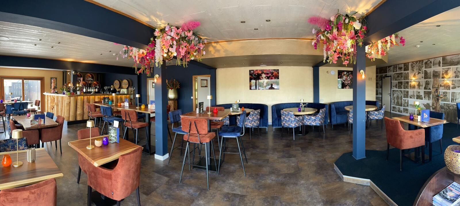 Een restaurant met ronde tafels en stoelen, een bar en decoratieve bloemstukken.