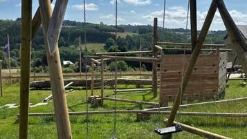 Un ensemble de balançoires en bois, installé dans un espace herbeux, avec une structure en bois en arrière-plan.