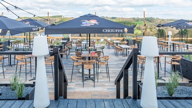 An outdoor patio area with multiple tables and chairs, covered by large umbrellas, and a view of the landscape. - Achouffe Valley (Houffalize)