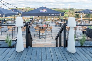 Un espace extérieur aménagé en terrasse, avec plusieurs tables et chaises, protégé par de grands parasols, et offrant une vue sur le paysage.