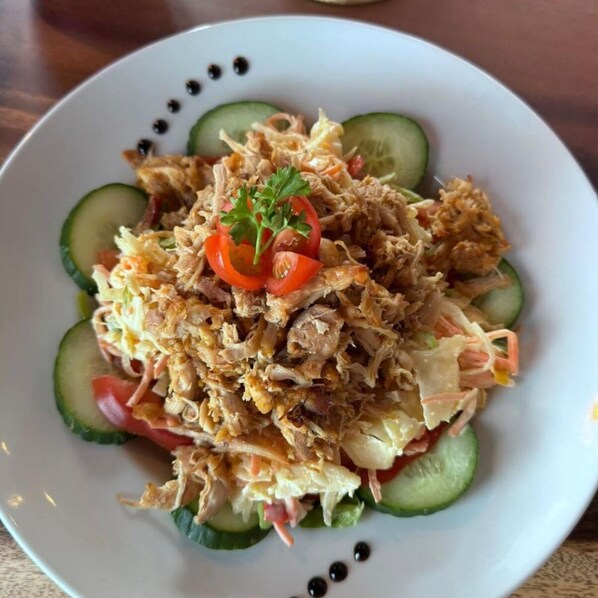 A plate of shredded chicken salad with cucumber slices and a garnish of red pepper and parsley. - Achouffe Valley (Houffalize)