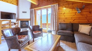 A cozy living room with wooden walls and ceiling, a fireplace, leather armchairs, a sofa, and a television. - Stunning Apartment With Mountain Views (Veysonnaz)