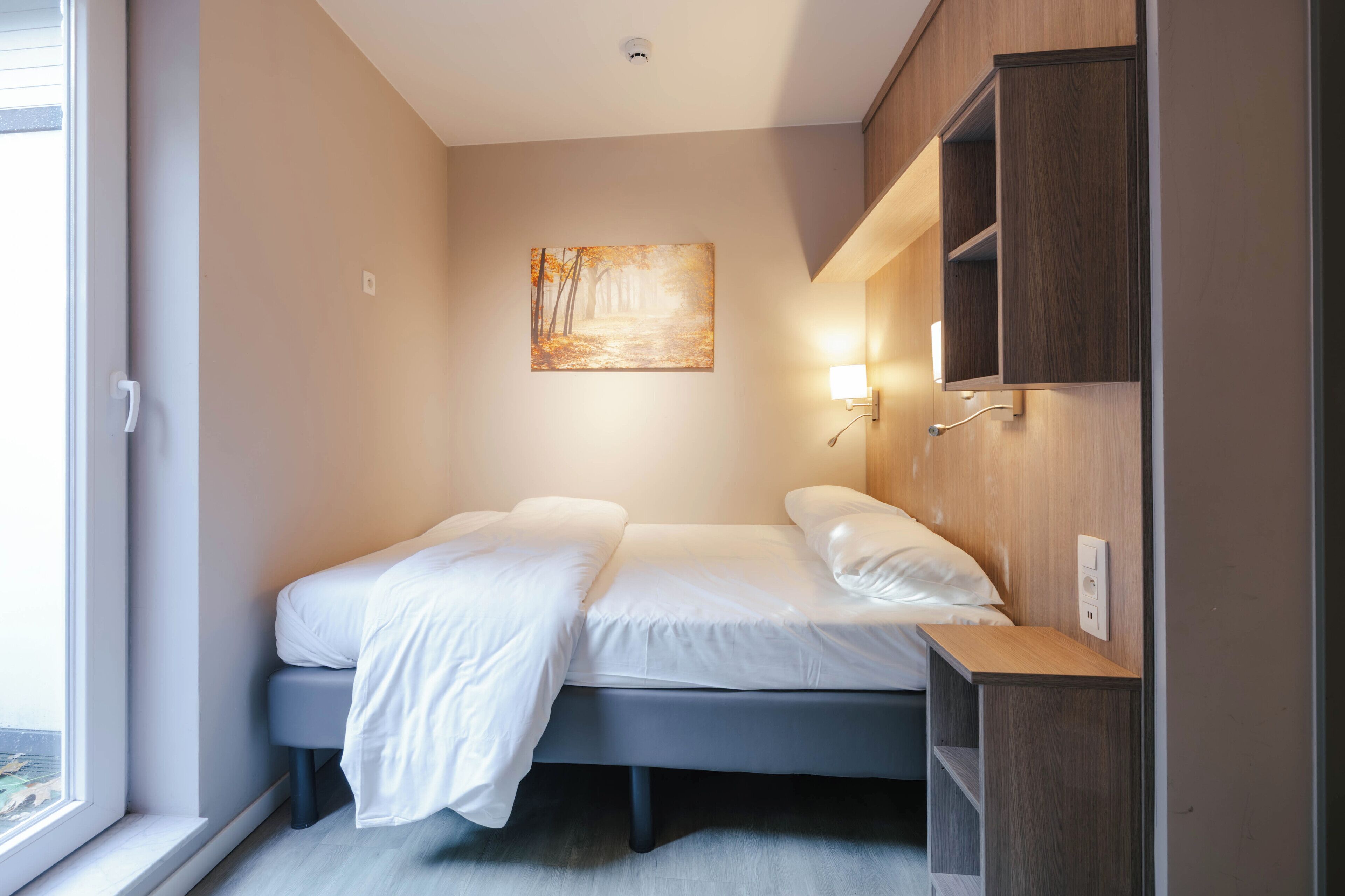 Un dormitorio con cama, mesita de noche y estante en la pared.