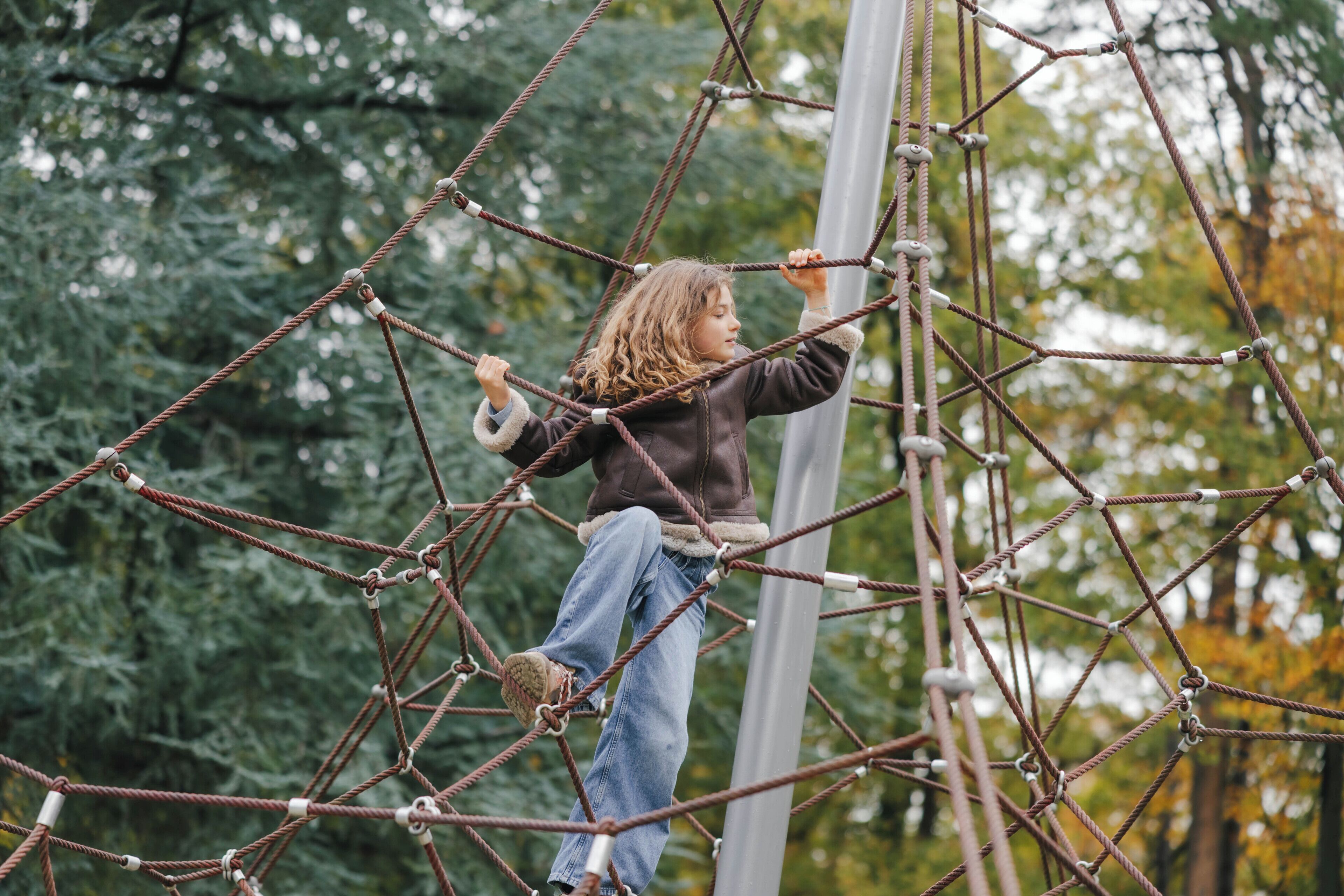 A person navigating a rope obstacle course in an outdoor setting with trees in the background.