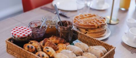 A breakfast buffet with pastries, waffles, and jams.