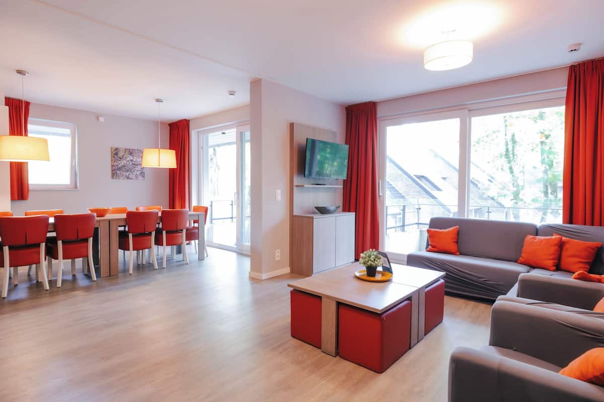 A modern living room with a sofa, a dining area with chairs, a coffee table, and a TV mounted on the wall.