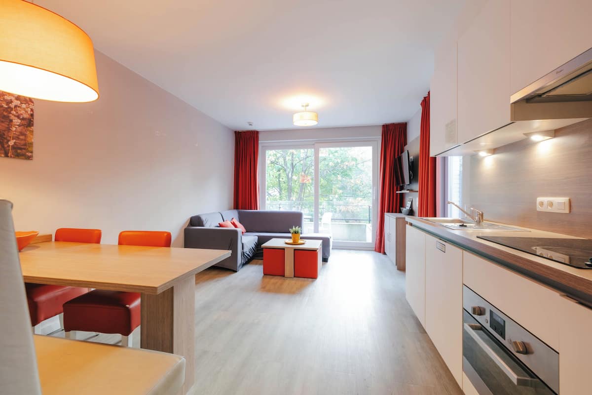 A modern apartment with a dining area, sofa, kitchen, and large windows.