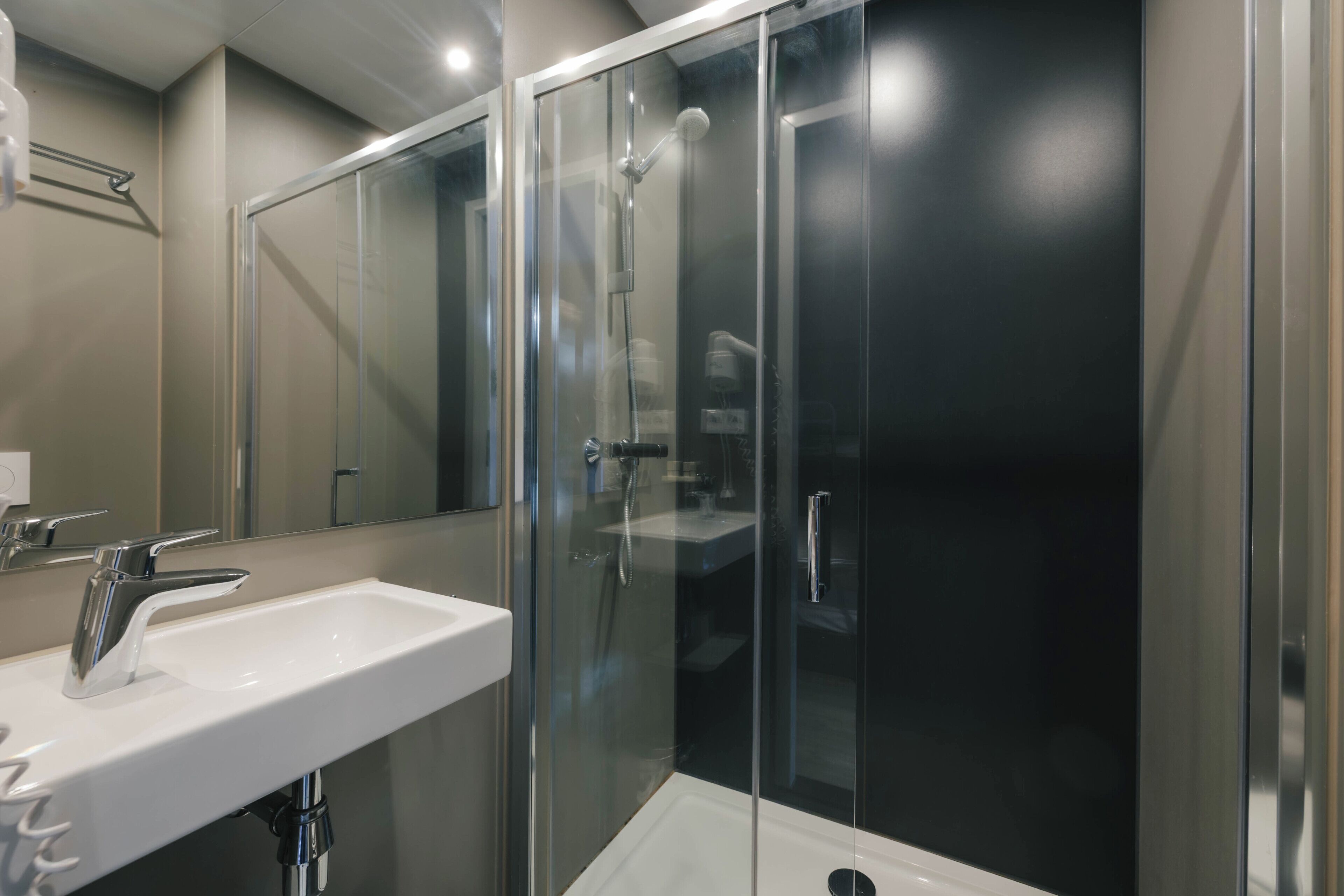 A modern bathroom with a glass-enclosed shower, a white sink, and a large mirror.
