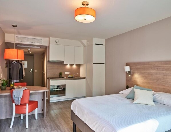 Una habitación de hotel compacta con cama, escritorio y kitchenette.