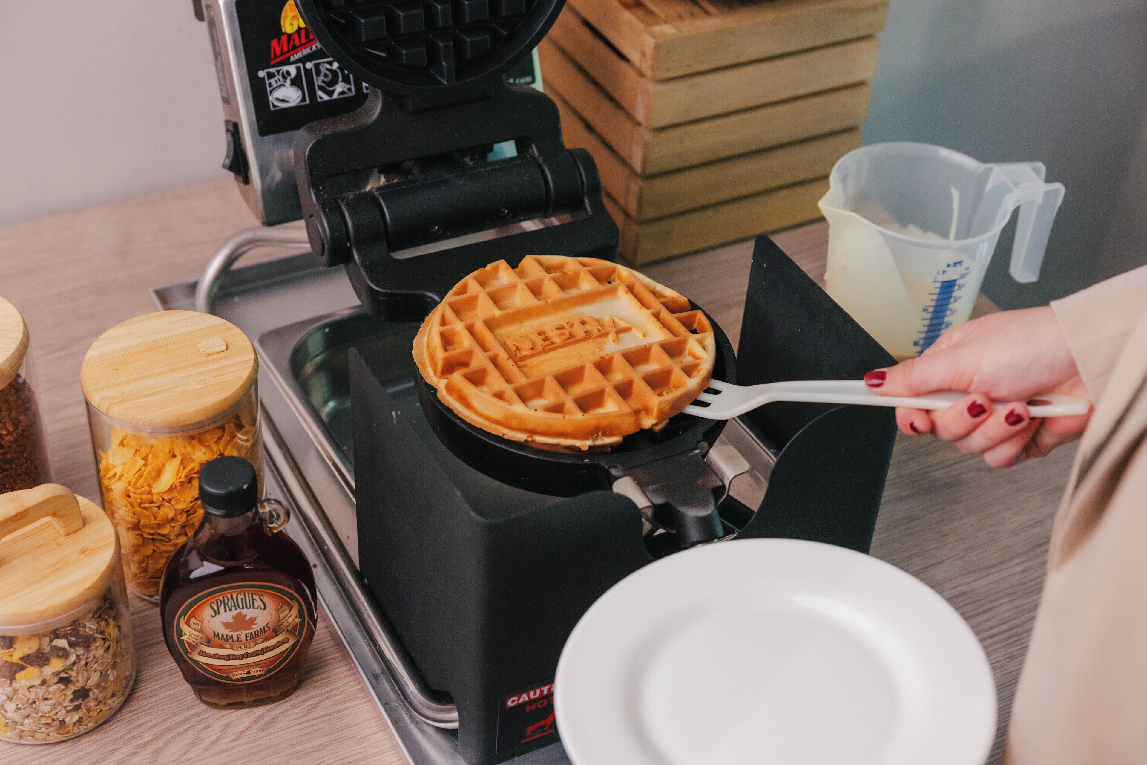 A waffle maker on a kitchen counter with a waffle being removed.
