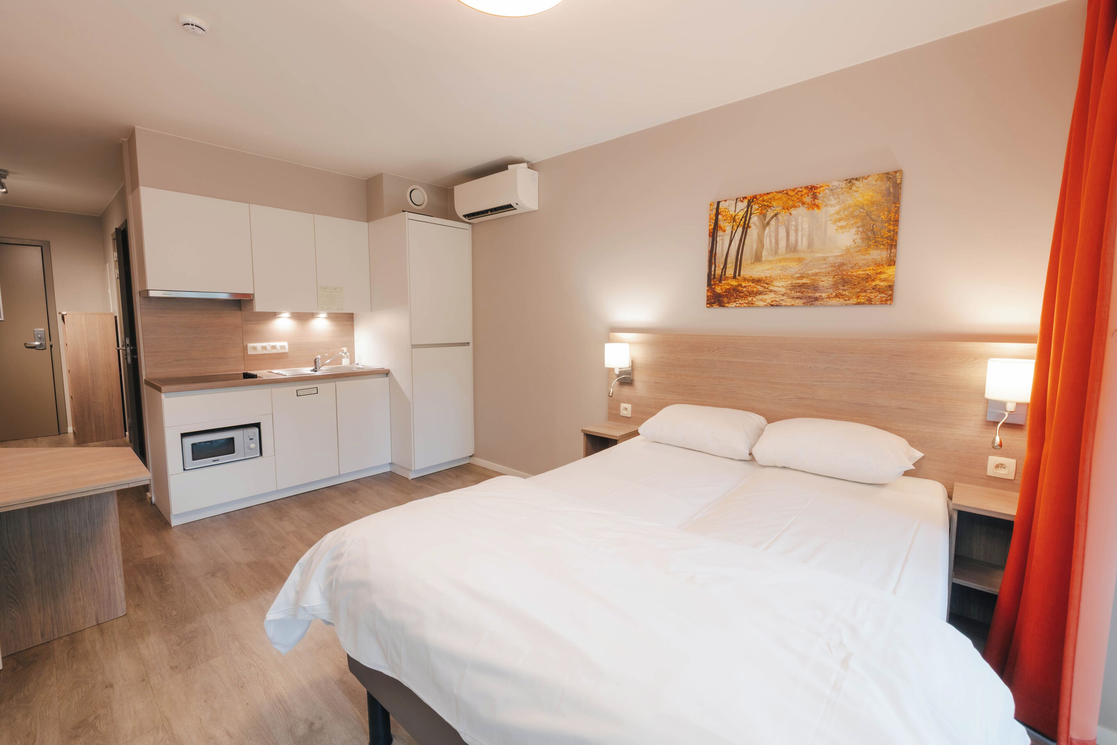Una habitación de hotel moderna con una cama grande, una kitchenette y un cuadro en la pared.