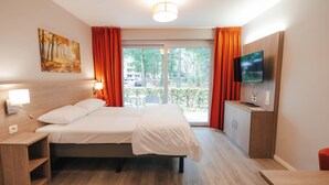 Moderni hotellihuone, jossa on sänky, televisio, työpöytä ja näkymä ulos.
