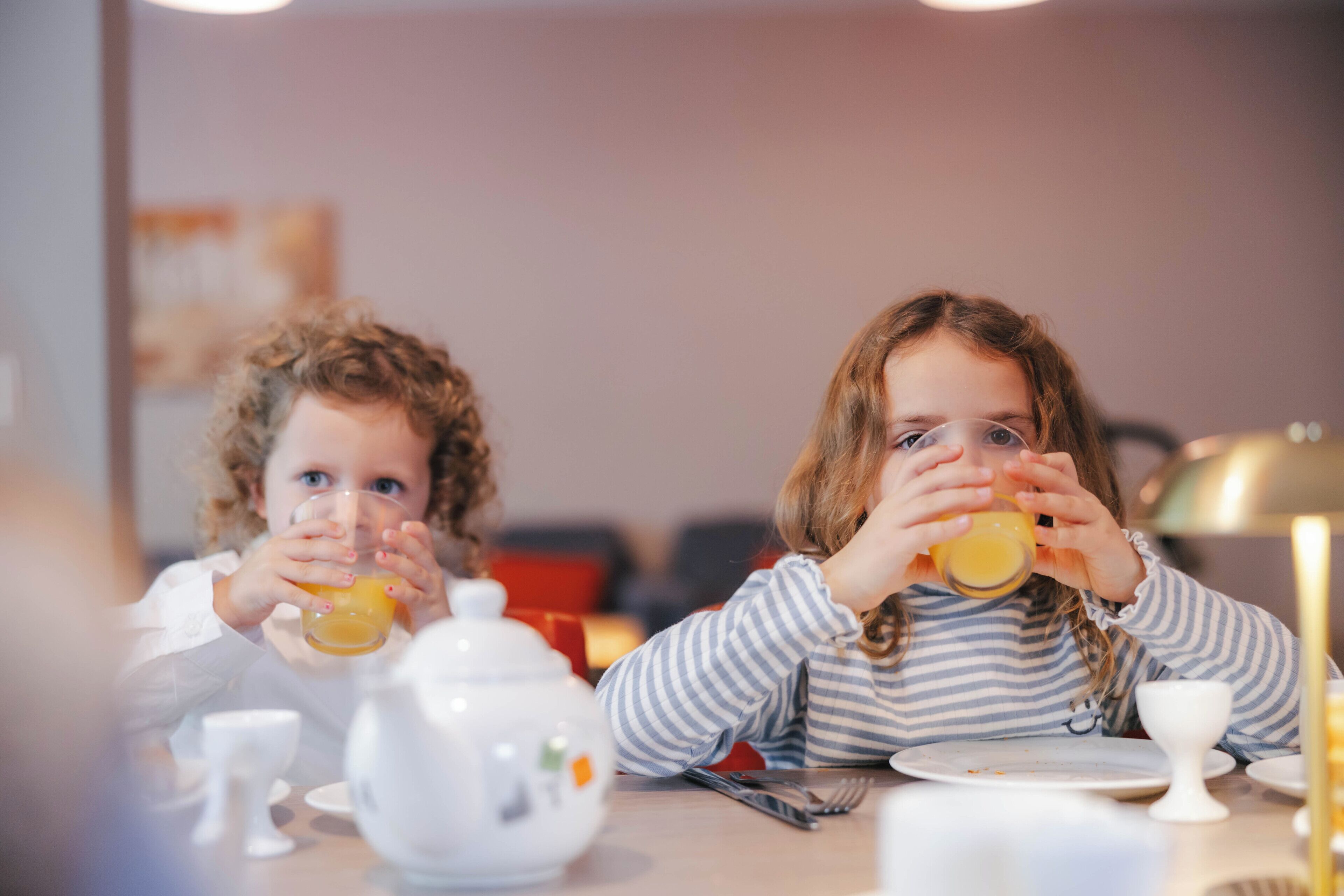 Two children sitting at a table with a teapot and cups, suggesting a dining area.