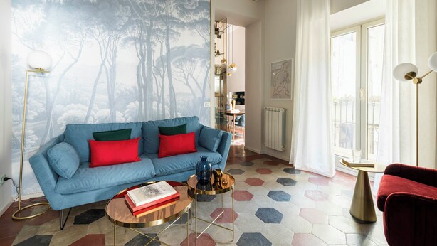 A living room with a blue sofa, red cushions, a round coffee table, and a hexagonal patterned floor. - Colosseo book house (Rome)