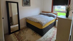 A bedroom with a bed, a mirror, a painting, a window with a view, and a ceiling light. - Apartmentsleeps5-parking-garden-petsok (Kelty)