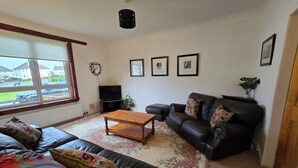 A living room with a sofa, a coffee table, a black leather couch, and a television. There are framed pictures on the wall and a plant on the floor. - Apartmentsleeps5-parking-garden-petsok (Kelty)