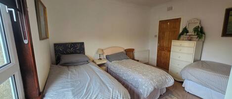 A bedroom with two single beds, a dresser, a radiator, and a window.