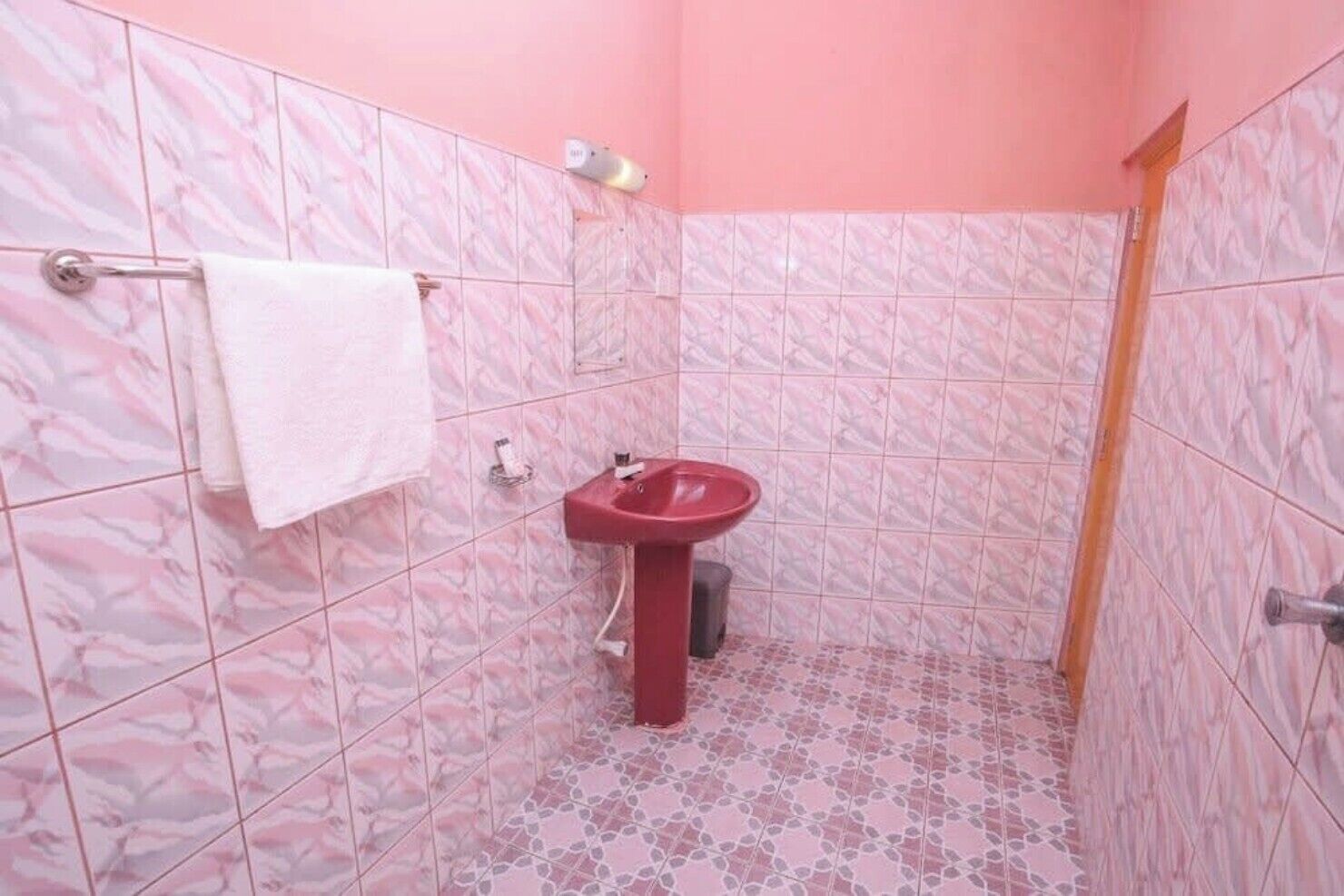A bathroom with pink marble tiles, a red sink, and a white towel on a rack.