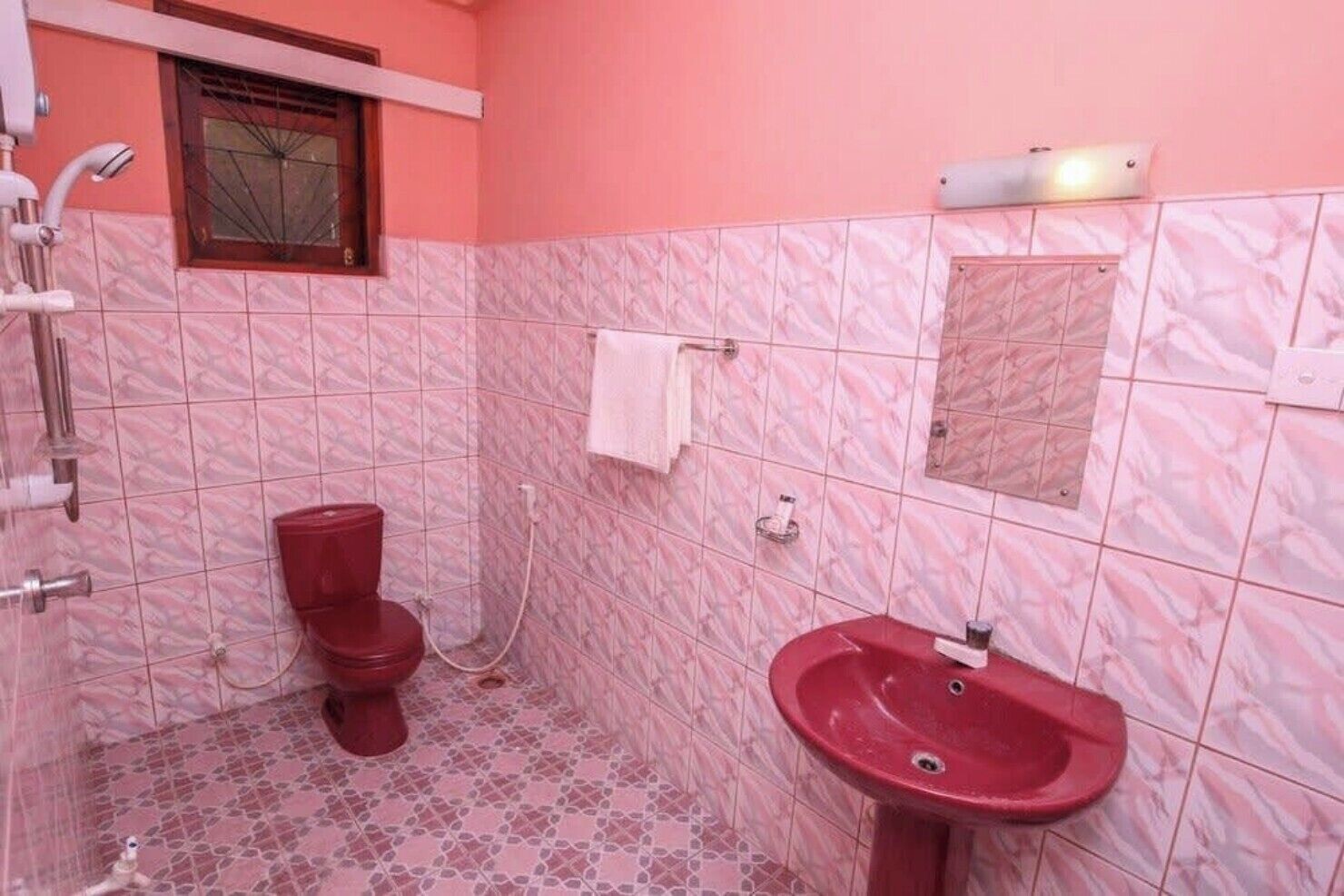 A bathroom with a red toilet, a sink, and a shower.