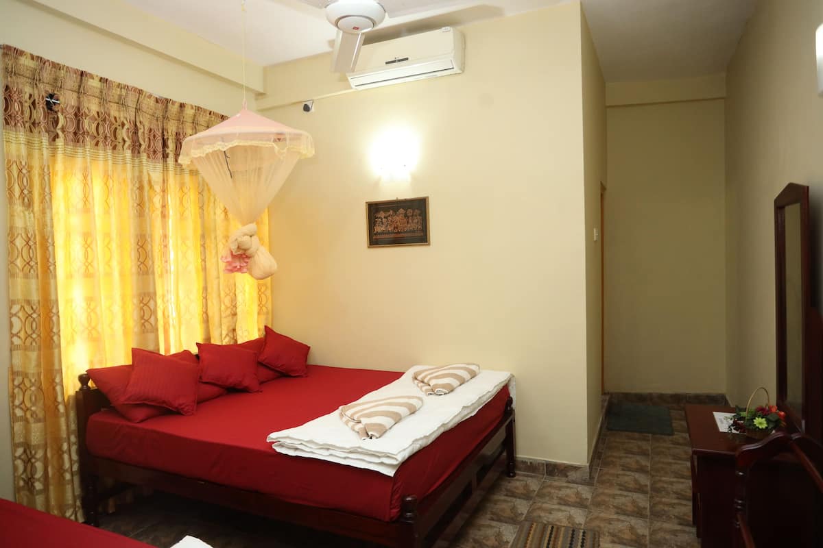 Habitación de hotel con cama, mesita de noche, espejo, aire acondicionado de pared y ventilador de techo.