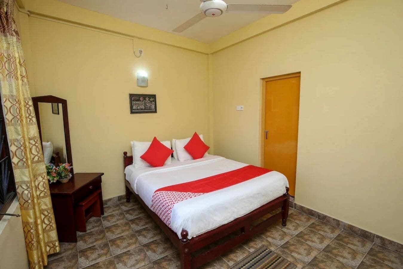 A bedroom with a bed, a wooden nightstand, a mirror, a door, and a ceiling fan.