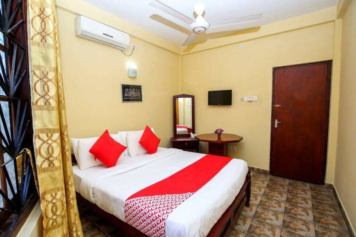 Habitación de hotel con cama, escritorio, silla, televisión, puerta y unidad de aire acondicionado.