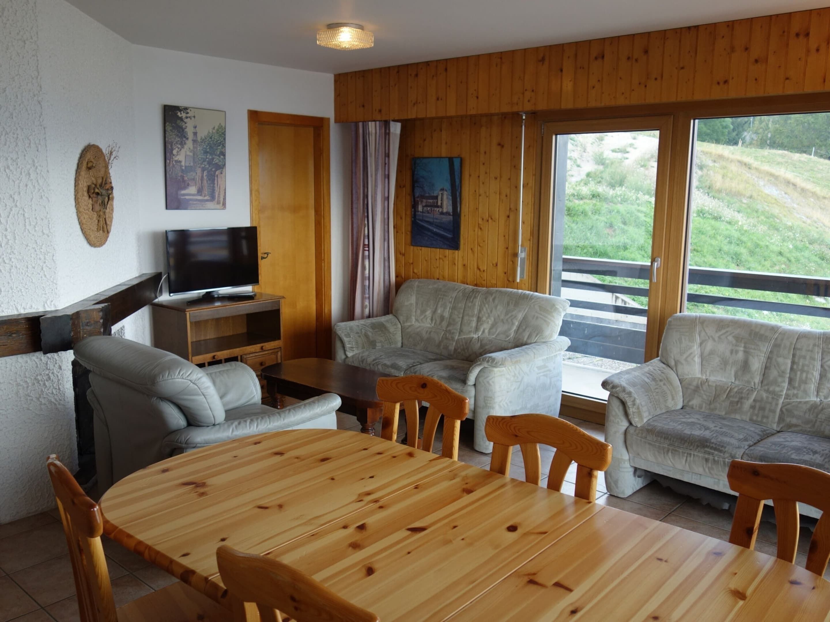A cozy living room with a wooden table, two sofas, a TV, and a painting on the wall.