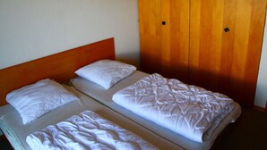 Una camera con due letti singoli, ognuno con biancheria da letto e cuscini bianchi, una testiera in legno e un armadio in legno a due ante.