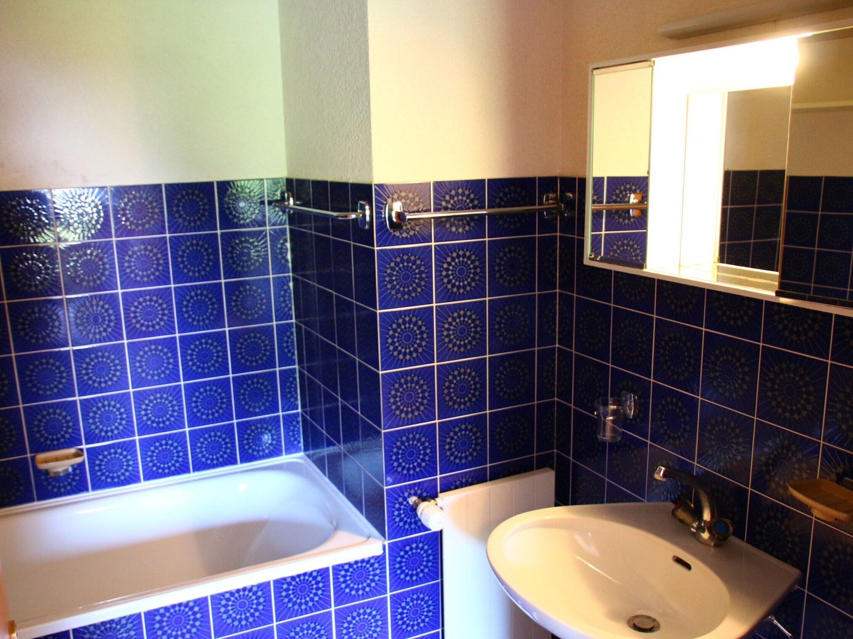 A bathroom with blue patterned tiles, a white sink, and a bathtub.
