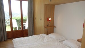 Un dormitorio con una cama, cabecera de madera, mesita de noche, lámpara de pared y puerta corrediza de vidrio que da a un espacio exterior.