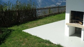 Un patio con una parrilla, cerca de madera y vistas a la montaña.