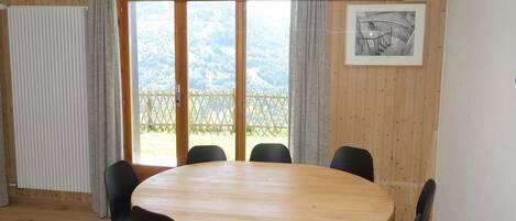 A conference room with a wooden table and black chairs, large windows with a view of a mountainous landscape, and a framed picture on the wall.