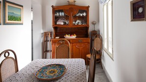 Een eethoek met een tafel gedekt voor twee personen, een houten kast met glazen deuren en een kroonluchter.
