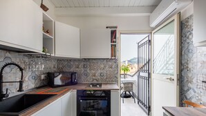 Een kleine keuken met een inbouwoven, een magnetron en een spoelbak. Er is een zithoekje met een stoel en een tafel.