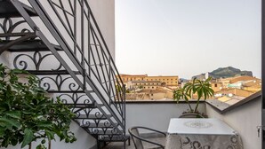 Een balkon met een tafel, stoelen en plantenbakken, en een metalen hekwerk.