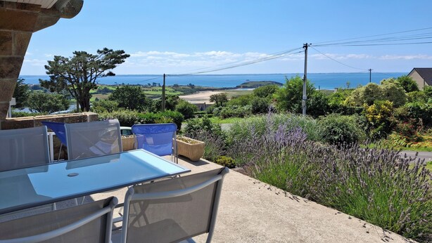 Un patio al aire libre con mesa y sillas, con vistas a un paisaje pintoresco y al mar y las colinas.