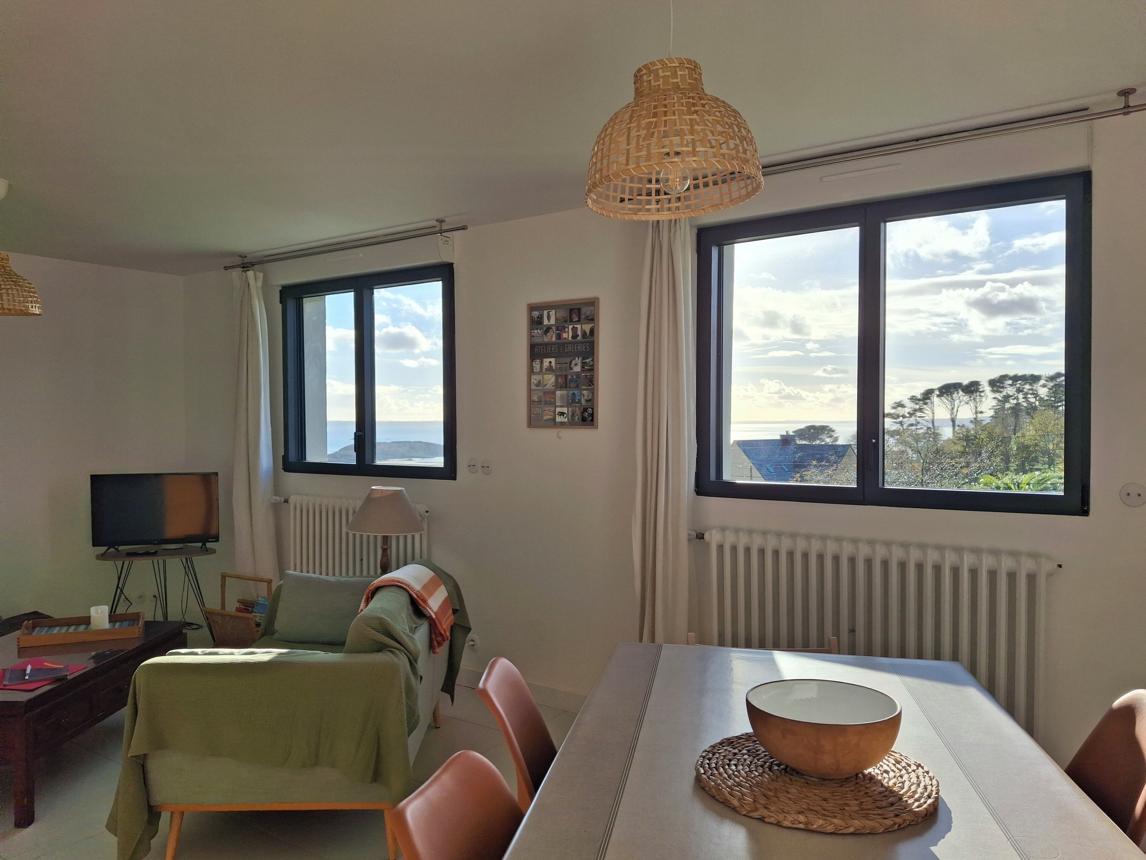 A dining area with a table, chairs, a television, and a view of the sea through large windows.
