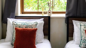 Una camera da letto con due letti, una finestra vista verde e un vaso decorativo sul davanzale.