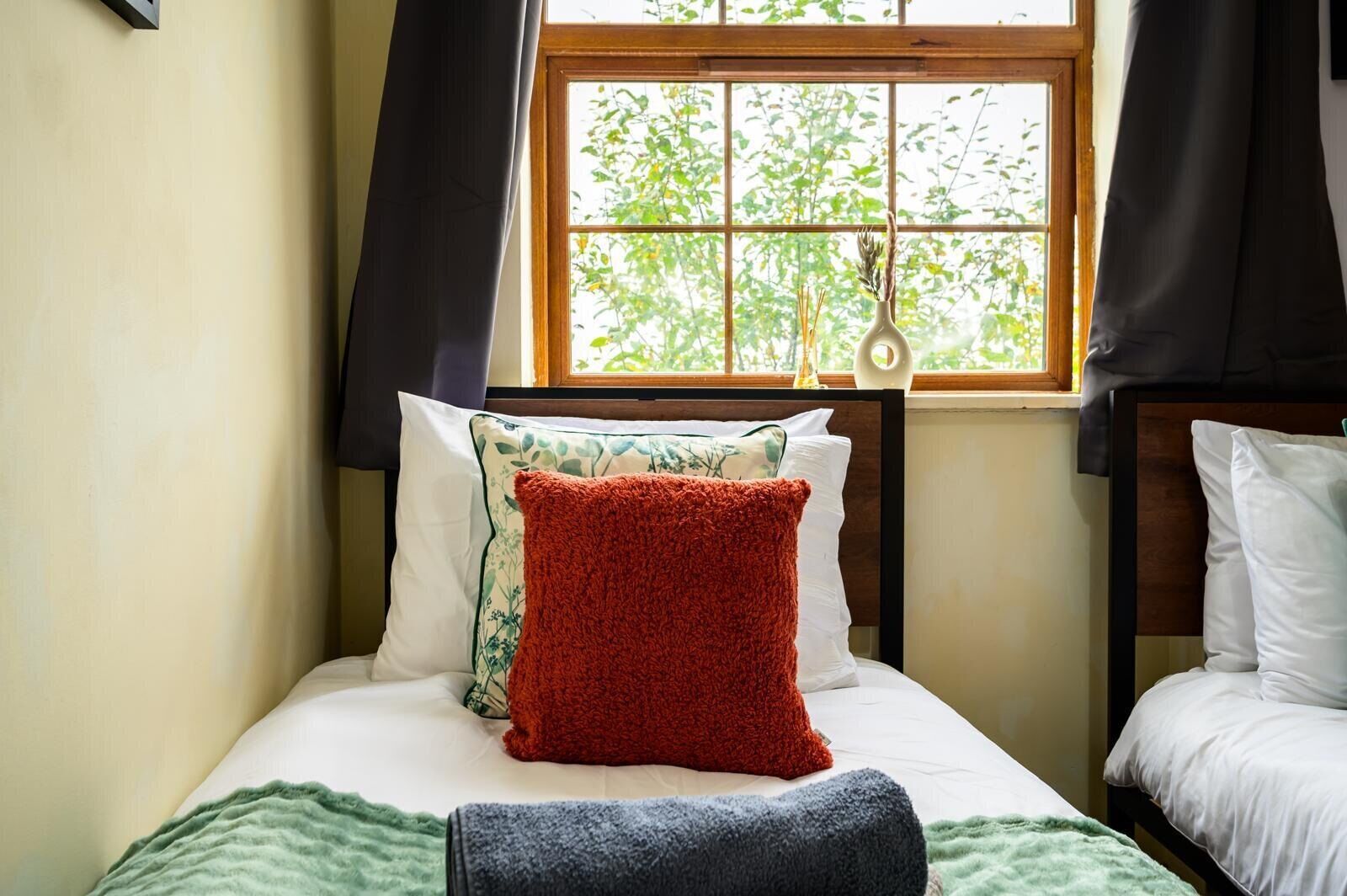 A bedroom with a bed, a window with a view of trees, and a bedside table with a lamp.