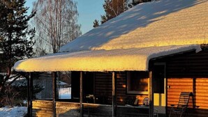 Una cabaña de madera con techo nevado y un porche.