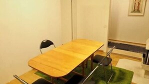 Una habitación pequeña y sencilla con una mesa de madera y cuatro sillas. Hay una alfombra verde en el suelo y un cuadro en la pared.