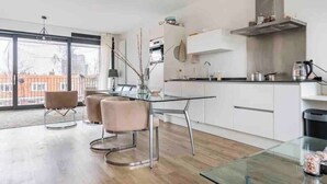 A modern kitchen with a glass dining table, white cabinets, and a large window overlooking a cityscape.