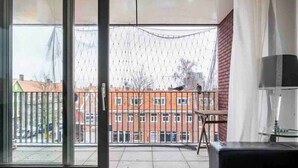 A room with a large sliding glass door leading to a balcony with a view of a brick building and a street.